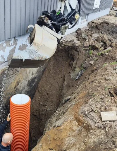 Bild på ett dräneringsarbete till ett småhus, där en man installerar den nya dräneringen.